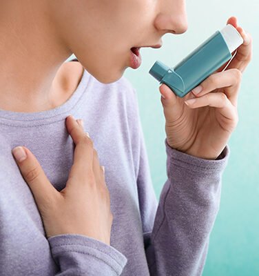 A person using an inhaler while holding their chest, indicating difficulty breathing or an asthma episode.