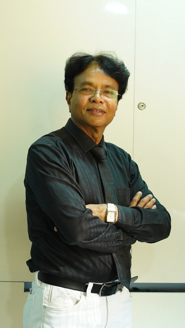 Dr. K. L. Prajapati poses confidently with a warm expression, dressed in a black formal shirt and tie.