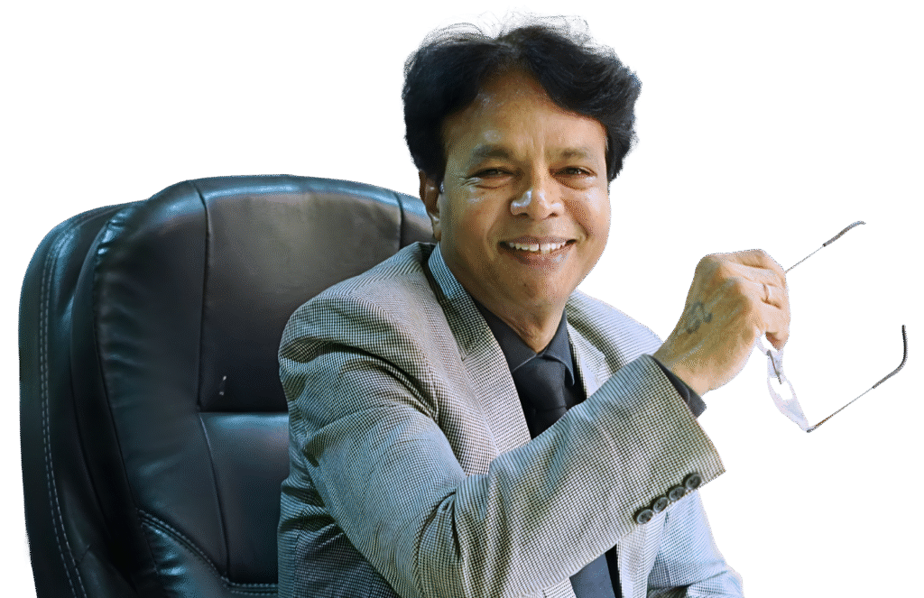 A man referred to by the user as Dr. K. L. Prajapati sitting in a leather office chair, smiling and holding a pair of eyeglasses while wearing a light gray blazer and black shirt–tie combination.