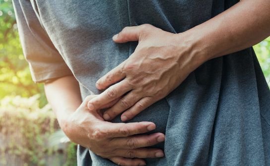 Person holding their abdomen with both hands, indicating stomach pain or discomfort.