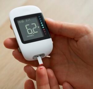 Person checking blood sugar level with a digital glucometer showing 6.2 mmol/L
