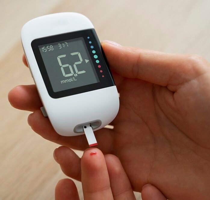 Person checking blood sugar level with a digital glucometer showing 6.2 mmol/L